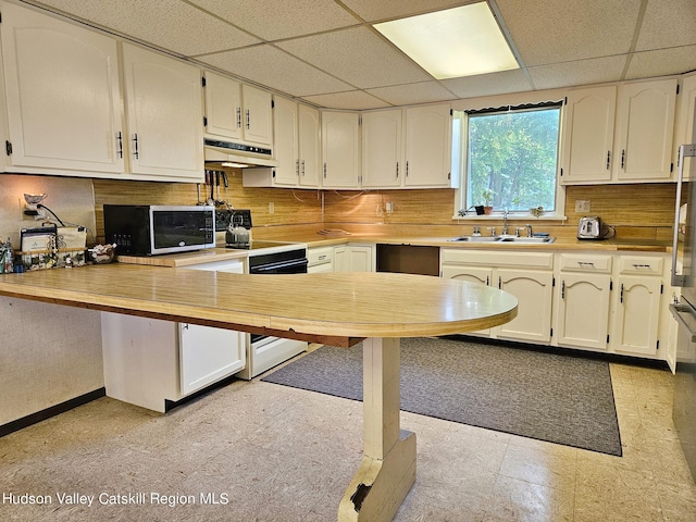 kitchen featuring kitchen peninsula, decorative backsplash, a drop ceiling, white range oven, and sink