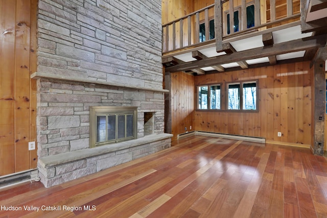 unfurnished living room with a fireplace, wooden walls, a baseboard radiator, and hardwood / wood-style floors