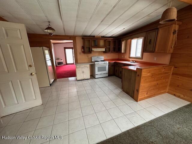 kitchen with hanging light fixtures, light tile patterned floors, wooden walls, and white appliances