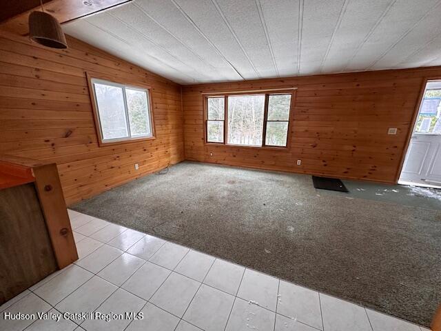 unfurnished room featuring light carpet, vaulted ceiling, and wood walls