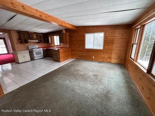 kitchen featuring light tile patterned flooring, a healthy amount of sunlight, white gas range, and wood walls