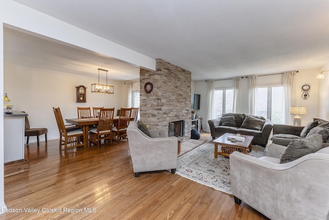 217 Aspen Ter, Poughkeepsie, NY 12601 - living room featuring an inviting chandelier, a textured ceiling, light wood-style flooring, and a stone fireplace