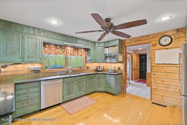 kitchen with wooden walls, light wood-type flooring, sink, and appliances with stainless steel finishes