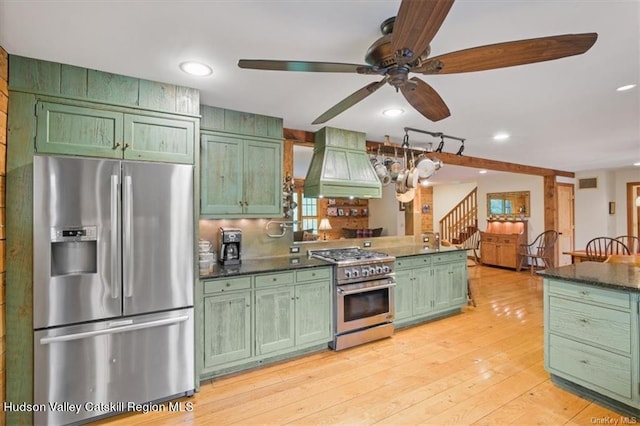 kitchen with appliances with stainless steel finishes, light wood-type flooring, custom range hood, ceiling fan, and green cabinetry