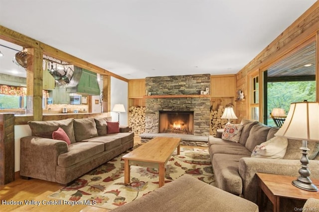 living room featuring a stone fireplace, wooden walls, a healthy amount of sunlight, and light wood-type flooring