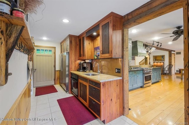 kitchen featuring appliances with stainless steel finishes, premium range hood, ceiling fan, sink, and light hardwood / wood-style flooring