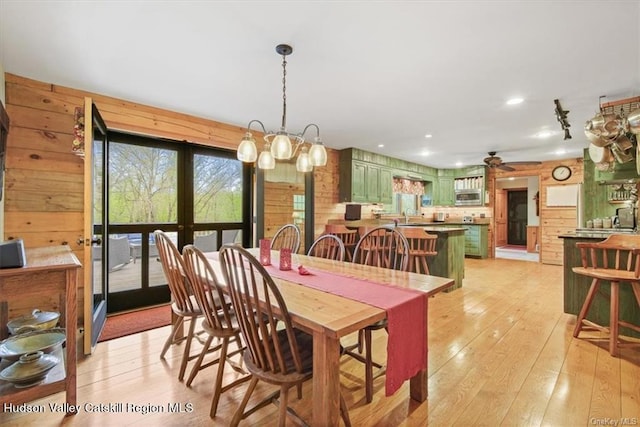 dining space featuring wooden walls, french doors, light hardwood / wood-style floors, and ceiling fan with notable chandelier