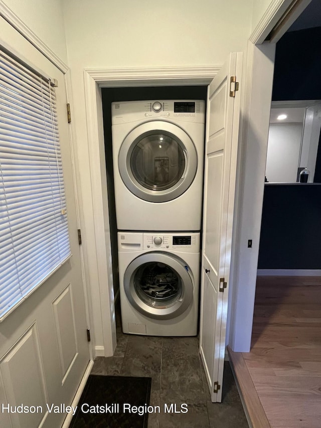 laundry area with stacked washer / dryer and dark tile patterned floors