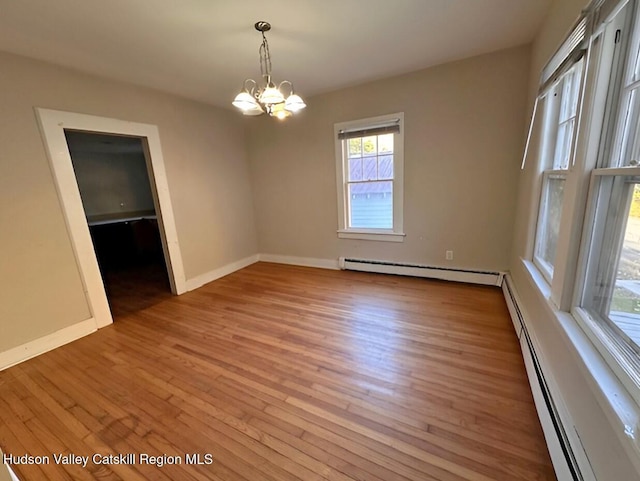 spare room with hardwood / wood-style flooring, a notable chandelier, and a baseboard heating unit