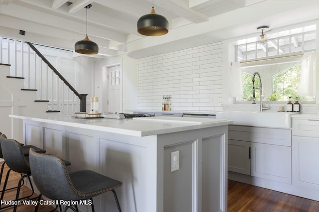 kitchen with pendant lighting, backsplash, dark hardwood / wood-style floors, light stone counters, and a kitchen bar