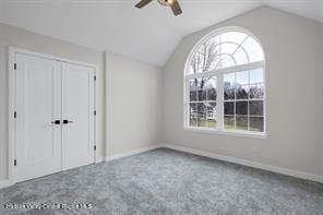 unfurnished bedroom featuring carpet floors, a closet, ceiling fan, and lofted ceiling