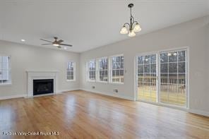 unfurnished living room with wood-type flooring, ceiling fan with notable chandelier, and a healthy amount of sunlight