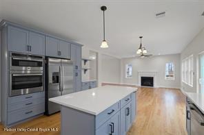 kitchen with a center island, hanging light fixtures, stainless steel fridge with ice dispenser, a fireplace, and double wall oven