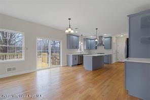 kitchen featuring wall chimney exhaust hood, a center island, a healthy amount of sunlight, and hanging light fixtures