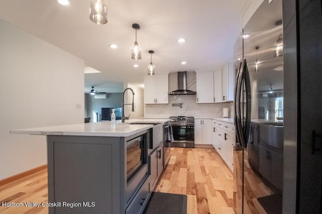 kitchen with white cabinets, wall chimney exhaust hood, light wood-type flooring, and appliances with stainless steel finishes