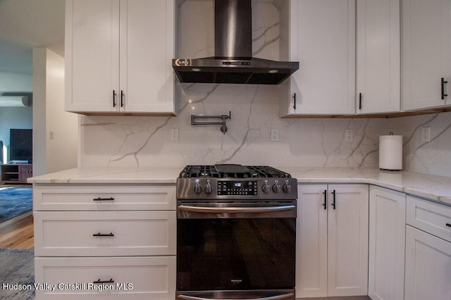 kitchen with gas range, wall chimney exhaust hood, light stone countertops, tasteful backsplash, and white cabinetry