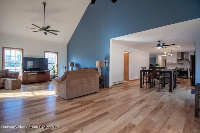 living room featuring light wood-type flooring, a baseboard radiator, high vaulted ceiling, and sink