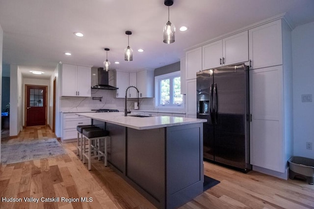 kitchen with wall chimney exhaust hood, light hardwood / wood-style floors, white cabinetry, and fridge with ice dispenser