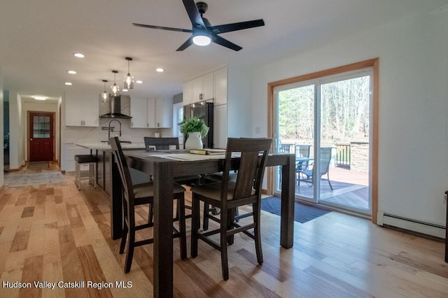 dining space with sink, light wood-type flooring, baseboard heating, and ceiling fan