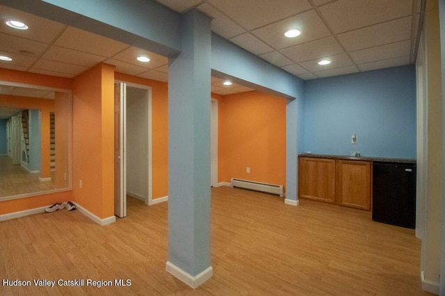 interior space with light wood-type flooring, a drop ceiling, and baseboard heating