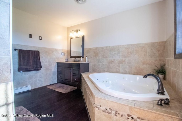 bathroom featuring a baseboard heating unit, tiled bath, hardwood / wood-style floors, vanity, and tile walls