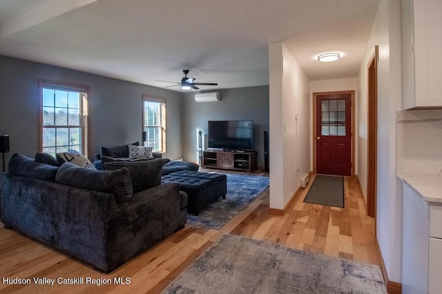 living room with a wall mounted air conditioner, ceiling fan, and light hardwood / wood-style floors