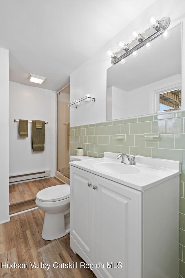 bathroom with a shower with shower door, a baseboard radiator, tile walls, vanity, and toilet