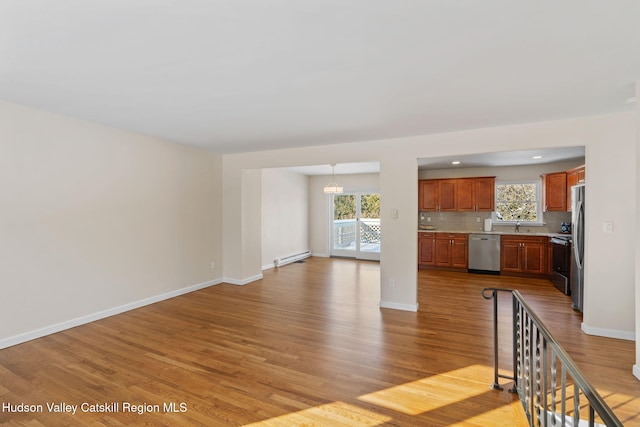 unfurnished living room with a baseboard radiator, sink, a notable chandelier, and light wood-type flooring