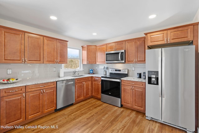 kitchen featuring sink, stainless steel appliances, light stone countertops, light hardwood / wood-style floors, and decorative backsplash