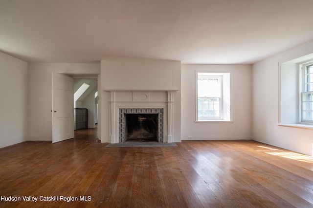 unfurnished living room with wood-type flooring and a tiled fireplace