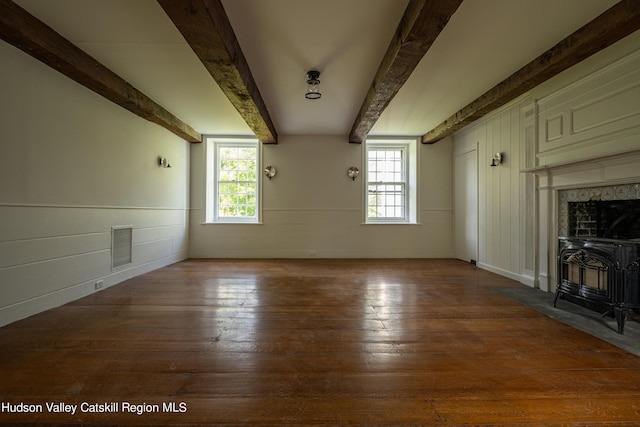 unfurnished living room with hardwood / wood-style floors, beam ceiling, a wood stove, and a wealth of natural light