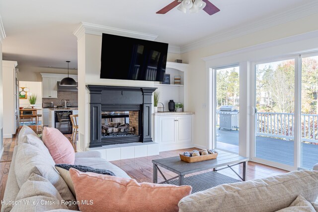 living room with ceiling fan, sink, light hardwood / wood-style floors, a fireplace, and ornamental molding