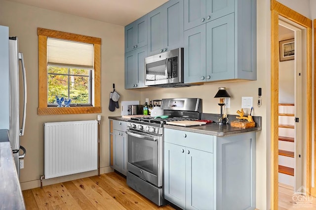 214 Fog Hill Rd, Austerlitz, NY 12017 - kitchen featuring radiator heating unit, stainless steel appliances, light wood-style flooring, dark countertops, and blue cabinets