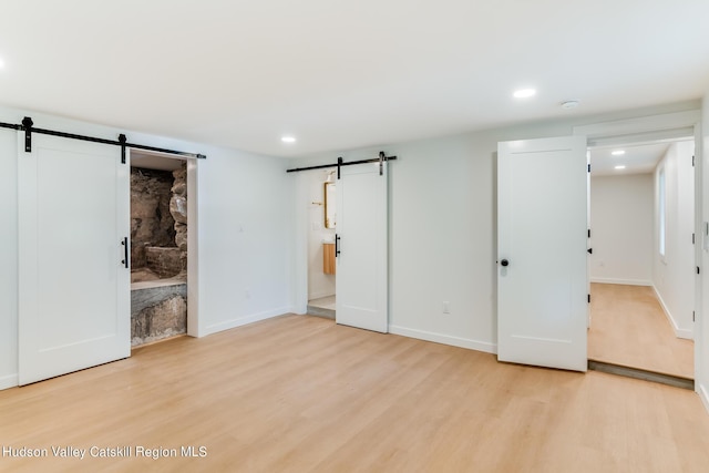 unfurnished bedroom with a barn door, connected bathroom, and light hardwood / wood-style flooring