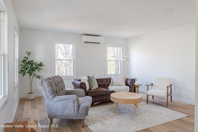 living room with a wall unit AC, a healthy amount of sunlight, and light wood-type flooring