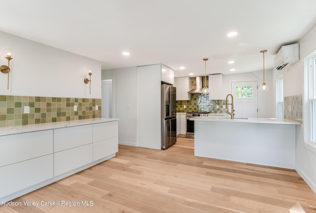 kitchen featuring white cabinets, wall chimney exhaust hood, decorative light fixtures, stainless steel appliances, and a wall unit AC