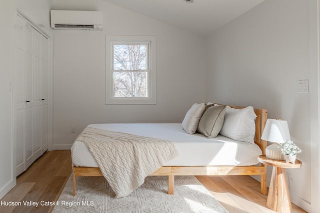 bedroom with a wall mounted air conditioner, vaulted ceiling, hardwood / wood-style floors, and a closet