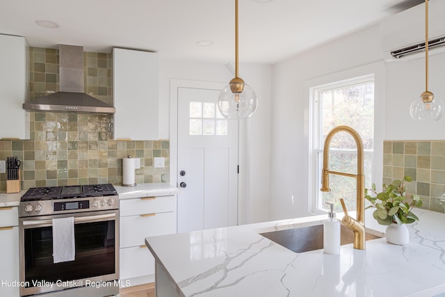 kitchen with pendant lighting, stainless steel gas stove, white cabinetry, and wall chimney range hood