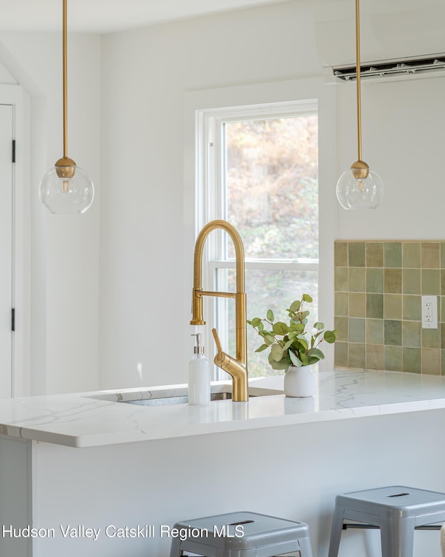 kitchen with backsplash, sink, hanging light fixtures, a wall mounted AC, and light stone counters