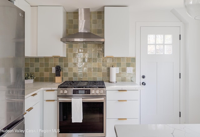 kitchen featuring light stone countertops, tasteful backsplash, stainless steel appliances, wall chimney range hood, and white cabinetry