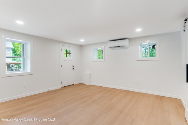 basement featuring a wealth of natural light, a barn door, light wood-type flooring, and a wall unit AC