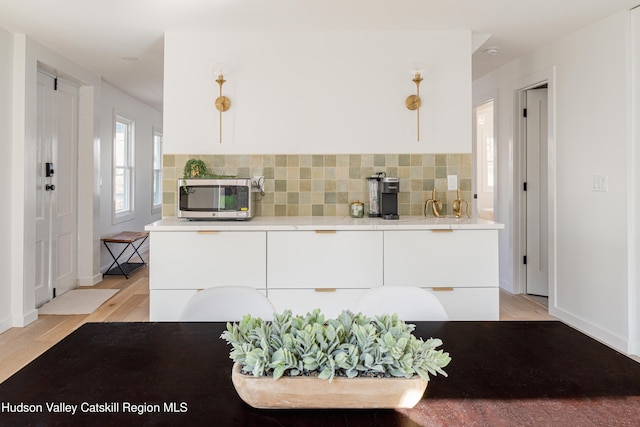 kitchen with white cabinets, decorative backsplash, and light wood-type flooring