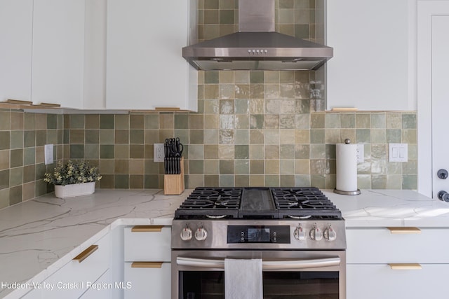 kitchen with high end range, light stone countertops, tasteful backsplash, wall chimney exhaust hood, and white cabinetry