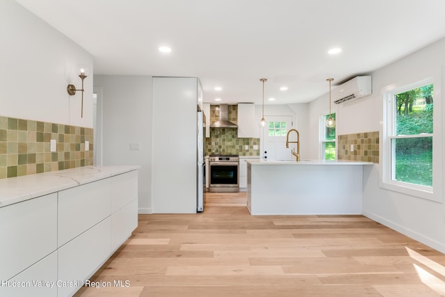 kitchen with decorative light fixtures, white cabinetry, stainless steel range oven, and wall chimney range hood