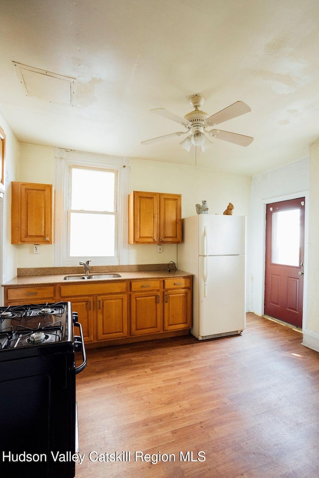 604 Columbia St, Hudson, NY 12534 - kitchen with black range with gas cooktop, freestanding refrigerator, a sink, brown cabinets, and light wood-style flooring