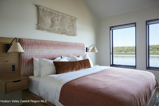 bedroom with hardwood / wood-style floors, a water view, and vaulted ceiling