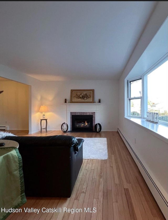 living room featuring a baseboard radiator, a brick fireplace, and hardwood / wood-style floors