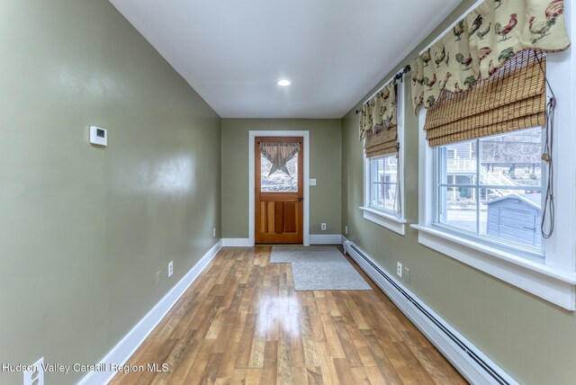 foyer entrance featuring a baseboard radiator, light wood-style flooring, and baseboards