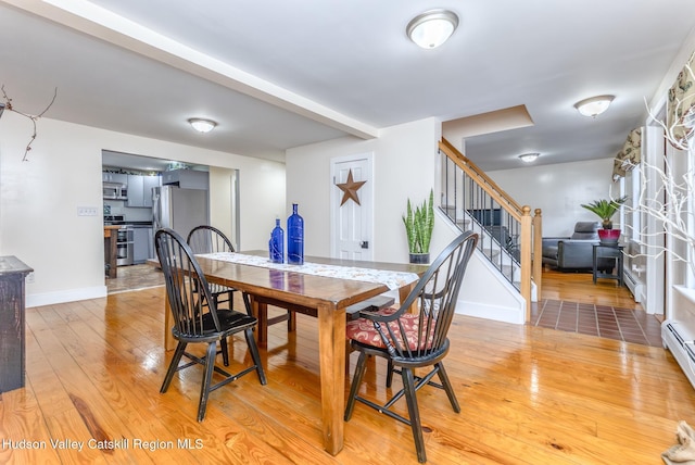 dining room featuring a baseboard heating unit, light wood-type flooring, baseboards, and stairs