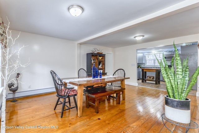 dining area with a baseboard heating unit, light wood-type flooring, and baseboards